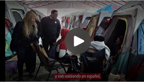 Grupo de personas conversando en un campamento con carpas, con un video en reproducción en primer plano.